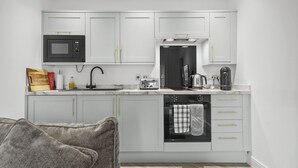 A compact kitchen with white cabinets, a microwave, a toaster, a kettle, and an oven. - The Snug | Beachwalk Apartments by Nova Suites (South Ayrshire)
