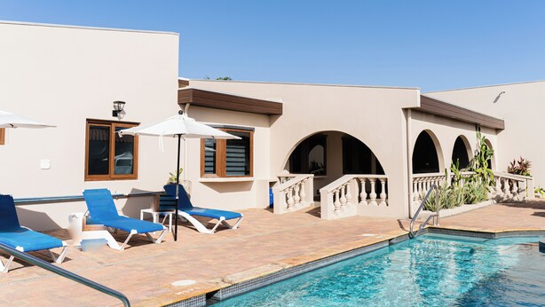 A pool area with blue lounge chairs, a tiled deck, and a clear blue pool. - Luxurious Villa 5 minutes from EAGLE BEACH (Noord)