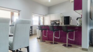 A modern kitchen with a purple accent wall, a bar area with stools, and a dining area with chairs. - Luxurious Villa 5 minutes from EAGLE BEACH (Noord)