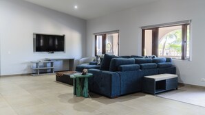 A modern living room with a large blue sofa, a small round table, and a flat-screen TV mounted on the wall. - Luxurious Villa 5 minutes from EAGLE BEACH (Noord)