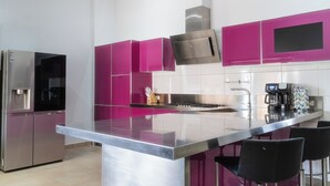 A modern kitchen with stainless steel appliances, a central island, and vibrant pink cabinets. - Luxurious Villa 5 minutes from EAGLE BEACH (Noord)