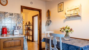 Une cuisine équipée d’un appareil à café, d’un grille-pain et d’une bouilloire sur le plan de travail, d’une table à manger agrémentée d’un vase de fleurs et d’un meuble en bois avec des tiroirs.