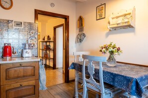 A kitchen with a coffee maker, toaster, and kettle on the counter, a dining table with a vase of flowers, and a wooden cabinet with drawers. - Apartment 'Casa Resi - Le Case di Quota' (Quota)
