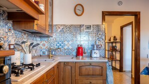 Une cuisine avec des meubles de rangement en bois, une cuisinière à gaz, une cafetière rouge et un dosseret carrelé.