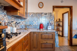 A kitchen with wooden cabinets, a gas stove, a red coffee maker, and a tiled backsplash. - Apartment 'Casa Resi - Le Case di Quota' (Quota)