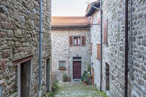 A narrow stone alleyway with a building featuring a wooden door and shutters, potted plants, and a tiled roof. - Apartment 'Casa Resi - Le Case di Quota' (Quota)