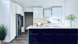 Una cocina moderna con armarios blancos, una isla central con taburetes y un refrigerador de acero inoxidable.