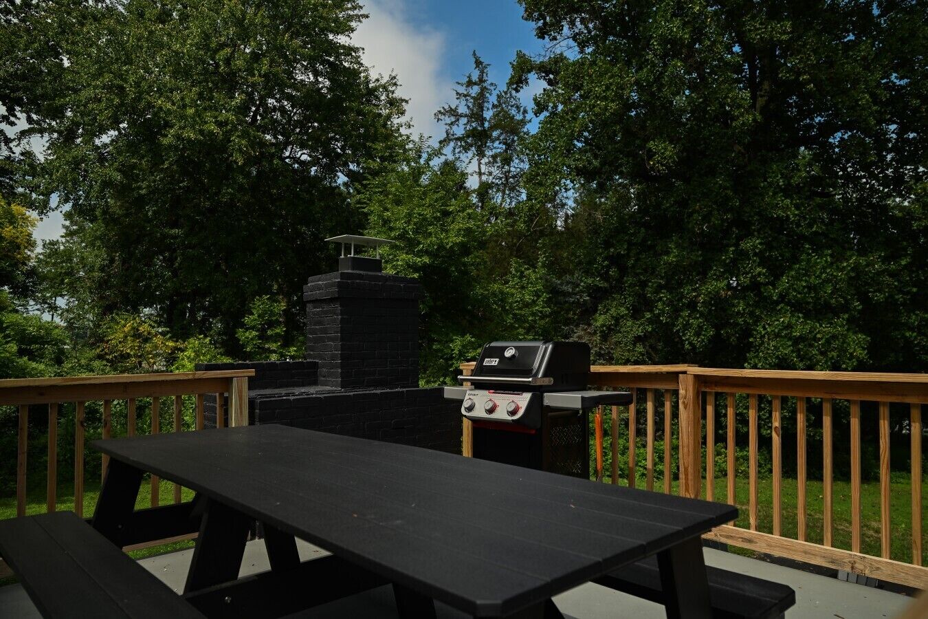 An outdoor deck with a grill and picnic table, surrounded by trees.