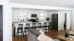 Une cuisine moderne avec des meubles blancs, un réfrigérateur en acier inoxydable et un îlot central doté de tabourets de bar.