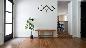Une pièce avec un plancher en bois, une plante en pot, un banc et un luminaire fixé au mur.