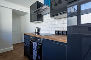 A modern kitchen with a wooden countertop, black cabinets, a stainless steel kettle, and labeled boxes for tea, sugar, and coffee.