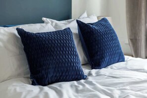 Ein Bett mit weißer Bettwäsche und zwei dunkelblauen Kissen.