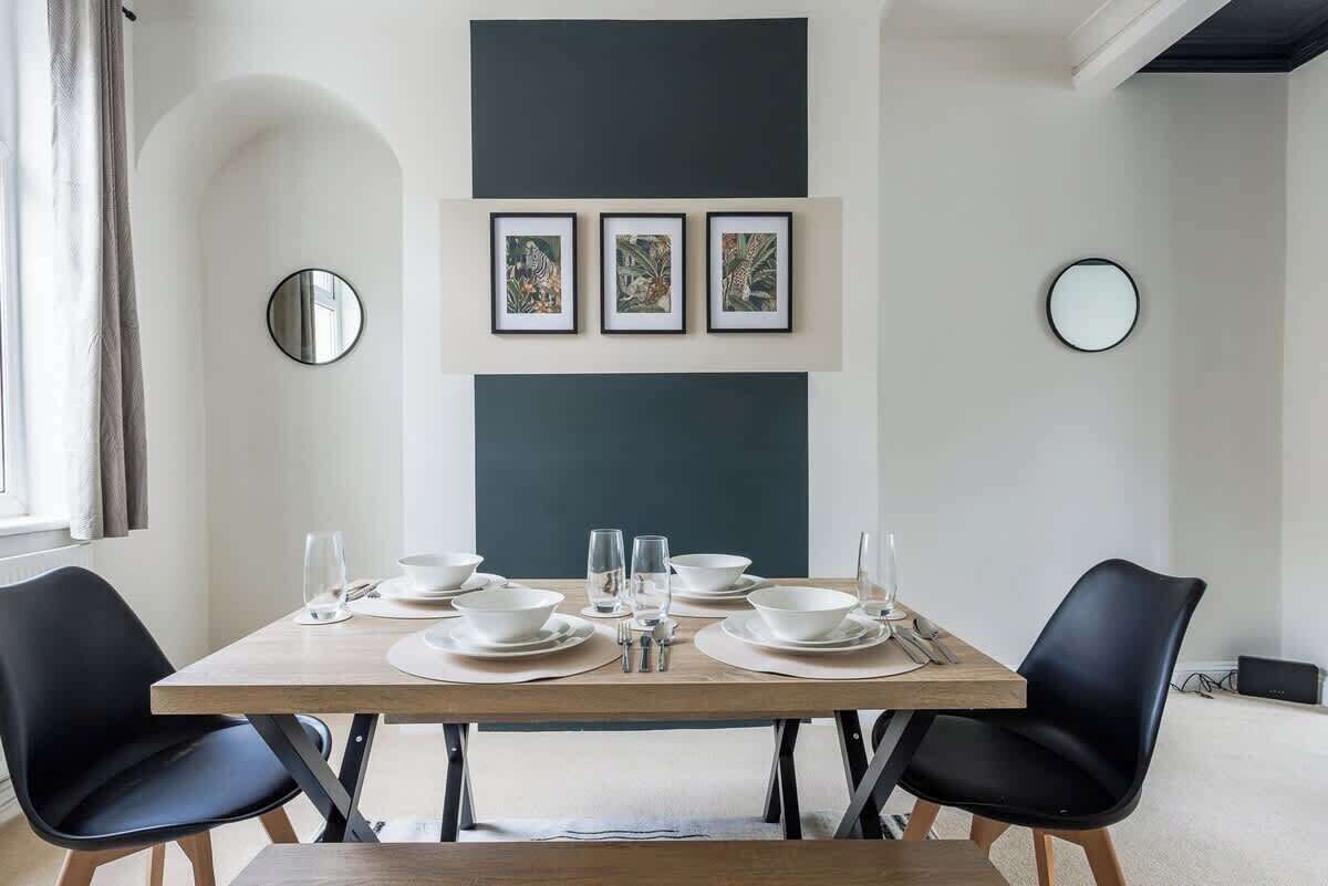 A dining area with a table set for four, framed artwork above, and a mirror on the wall.