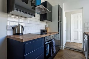 A modern kitchen with a wooden countertop, black cabinets, and a stainless steel kettle. - Comfortable 3 Bedroom House With WiFi (Stockton-on-Tees)