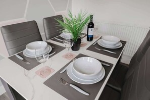 A dining table set with plates, bowls, wine glasses, and cutlery, accompanied by a potted plant and a bottle of wine.