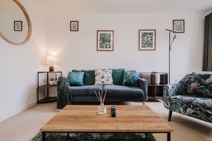 A living room with a sofa, a coffee table, and a floor lamp. - Modern and comfortable 3 bed house (Bedford)