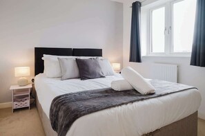 A neatly made bed with a dark headboard, white bedding, and a folded towel on the side.