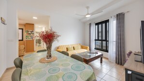 A living room with a round table, a sofa, a ceiling fan, and a view of the outside through a window.