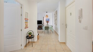 A hallway with a dining area at the end, featuring a table with chairs, a hanging light fixture, and a wall-mounted phone.