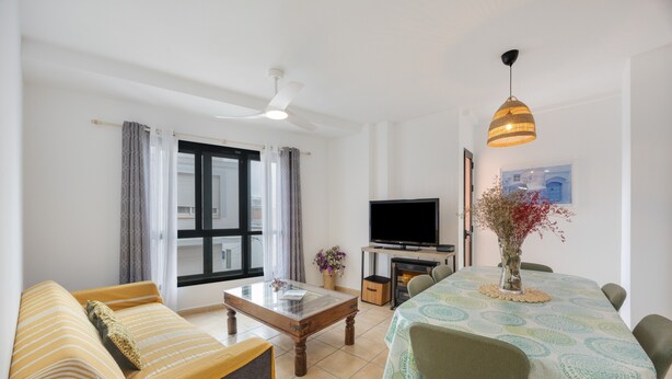 A living room with a sofa, a coffee table, a TV, and a dining table with chairs.