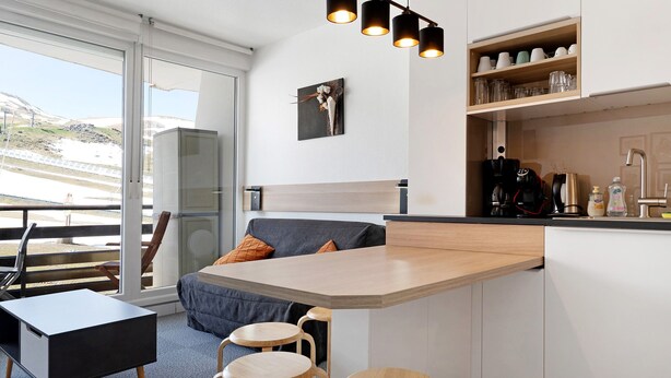 A modern kitchen with a breakfast bar, wooden stools, a coffee machine, and a view of the outdoors.