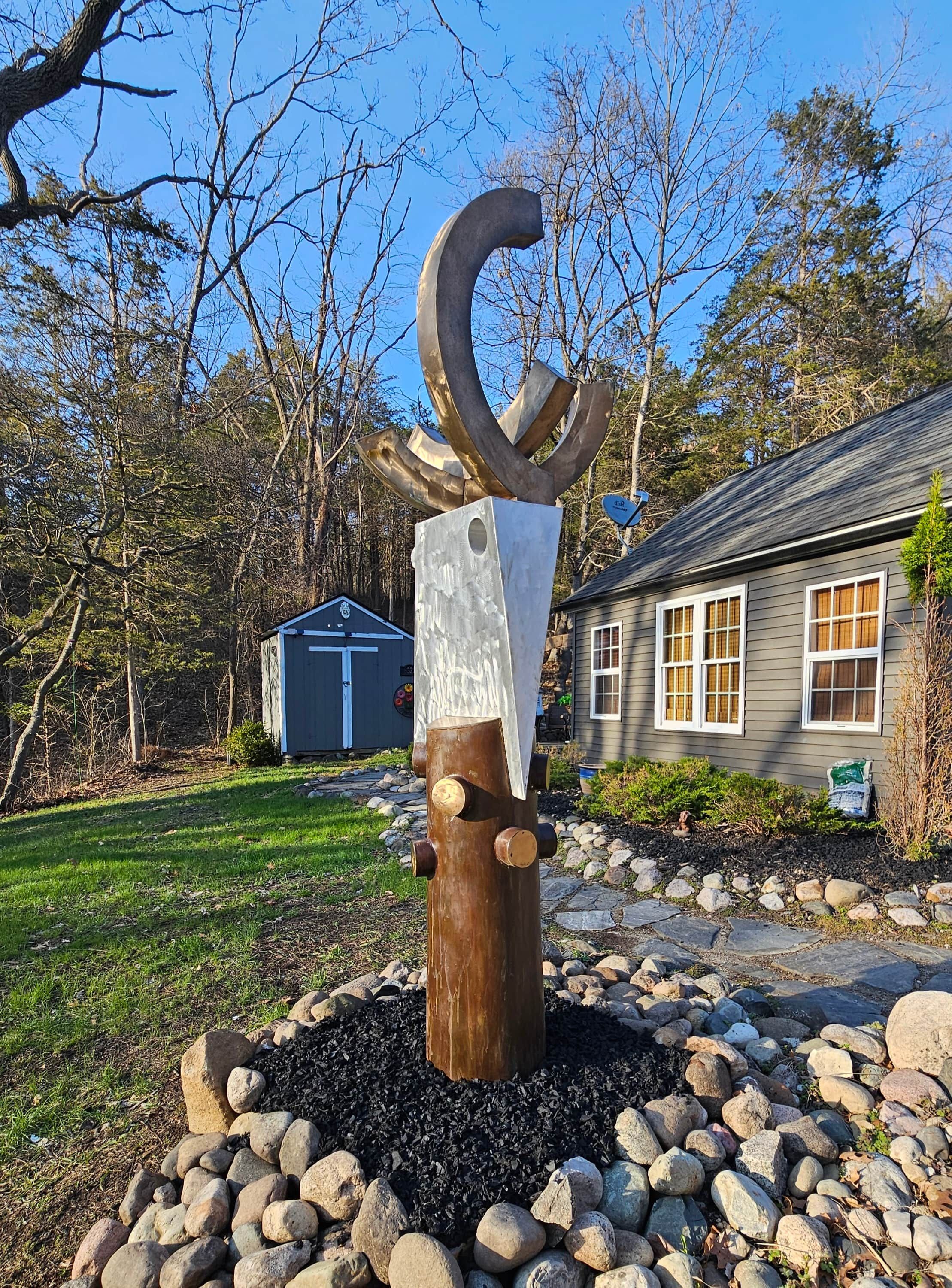 A sculpture in a garden with a house and shed in the background.