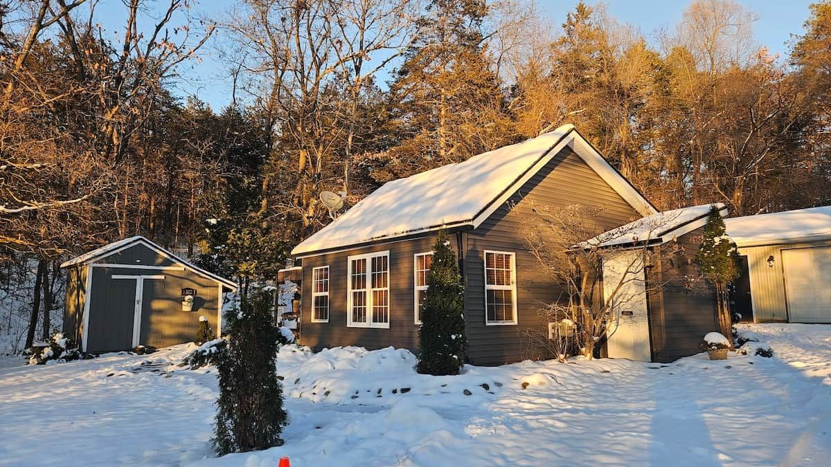 Una casa a due piani con tetto imbiancato dalla neve, circondata da alberi e un cielo sereno.