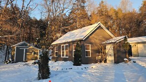 Une maison à deux étages, dont le toit est recouvert de neige, entourée d’arbres et sous un ciel dégagé.