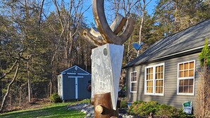 Una escultura en un jardín con una casa y un cobertizo al fondo.