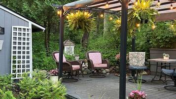 Een terras buiten met een pergola, zithoek en potplanten.