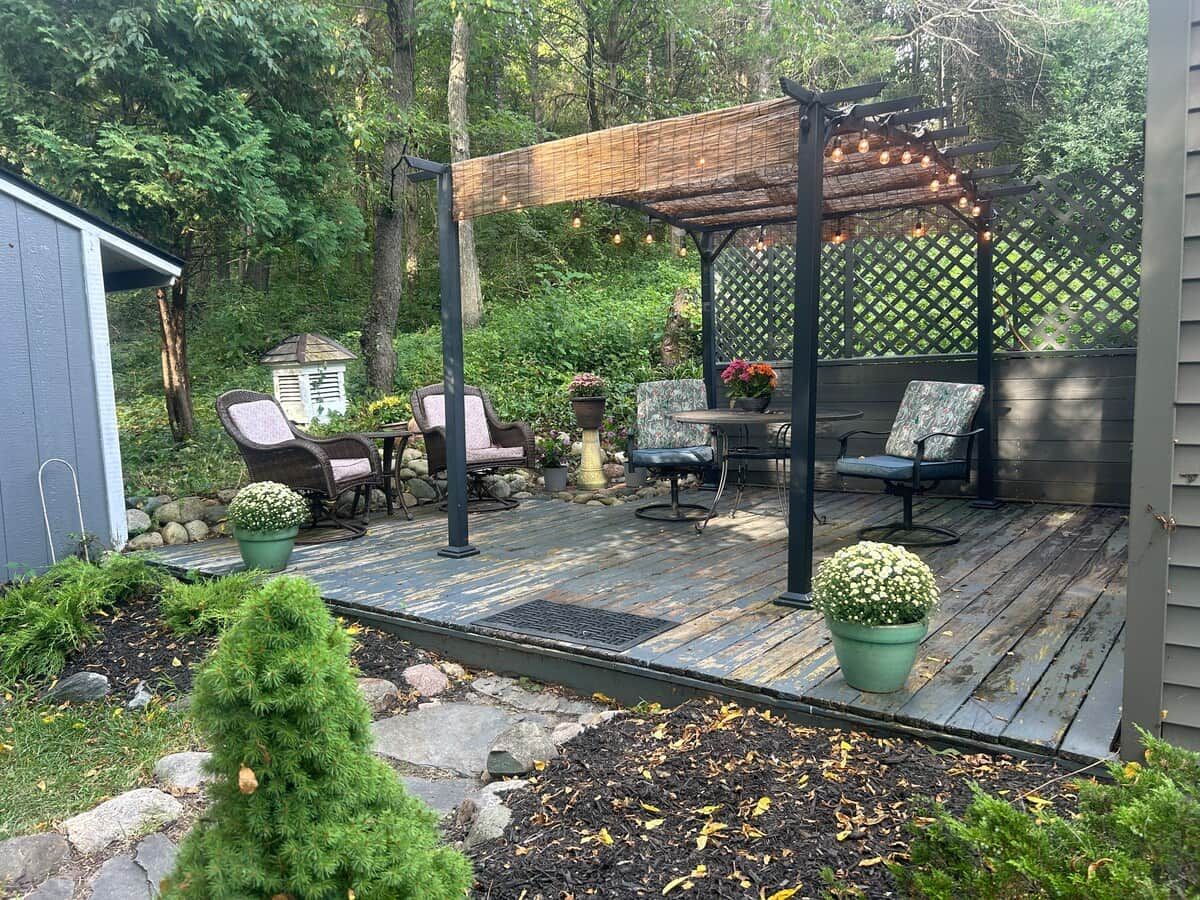 A wooden deck with outdoor furniture, a pergola with string lights, and a garden area with potted plants.