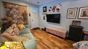 A living room with a wooden floor, a sofa, a pink bench, a TV, and a door with a window.
