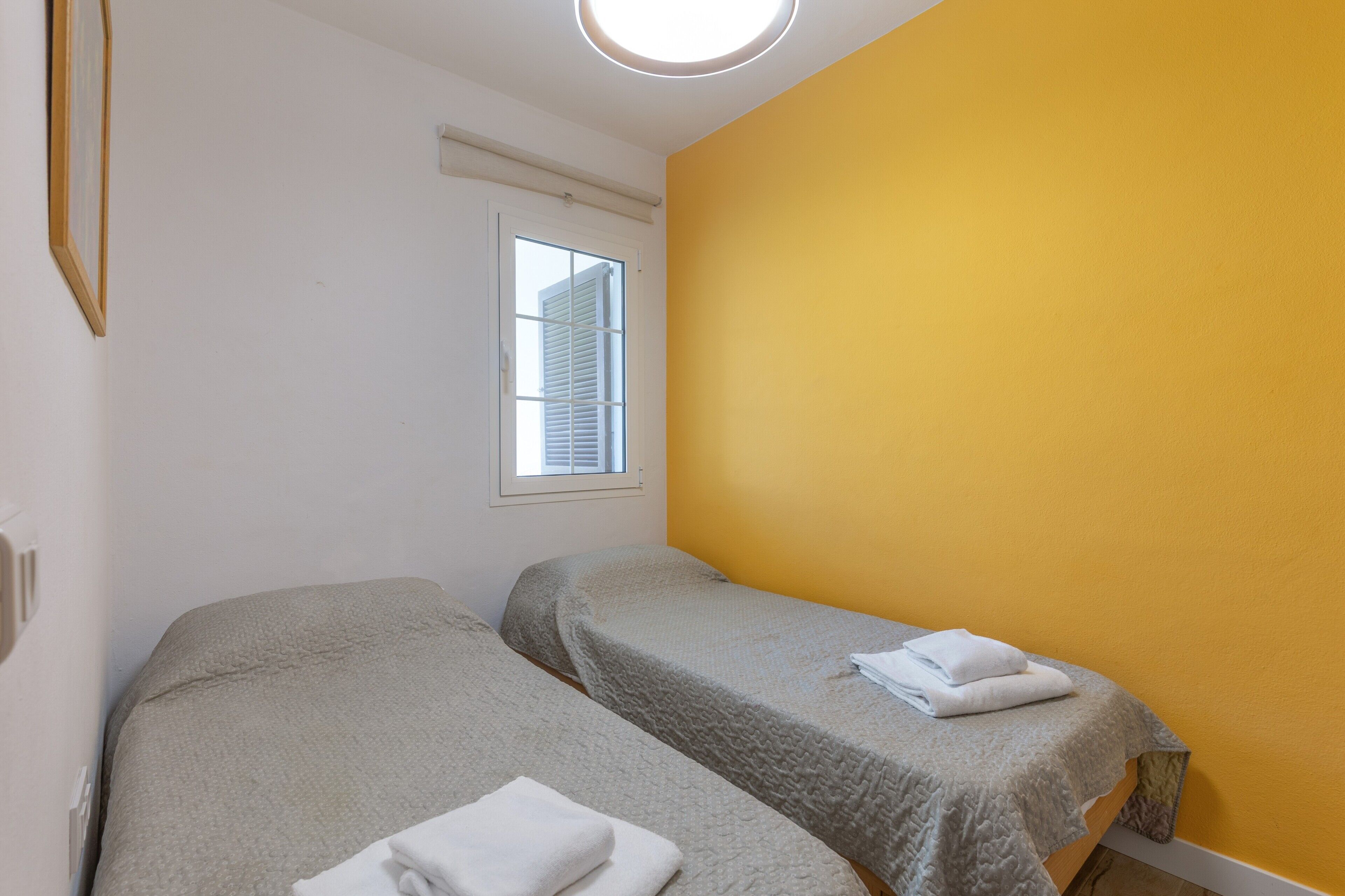 Una habitación con dos camas individuales, una ventana con persianas y una pared amarilla.