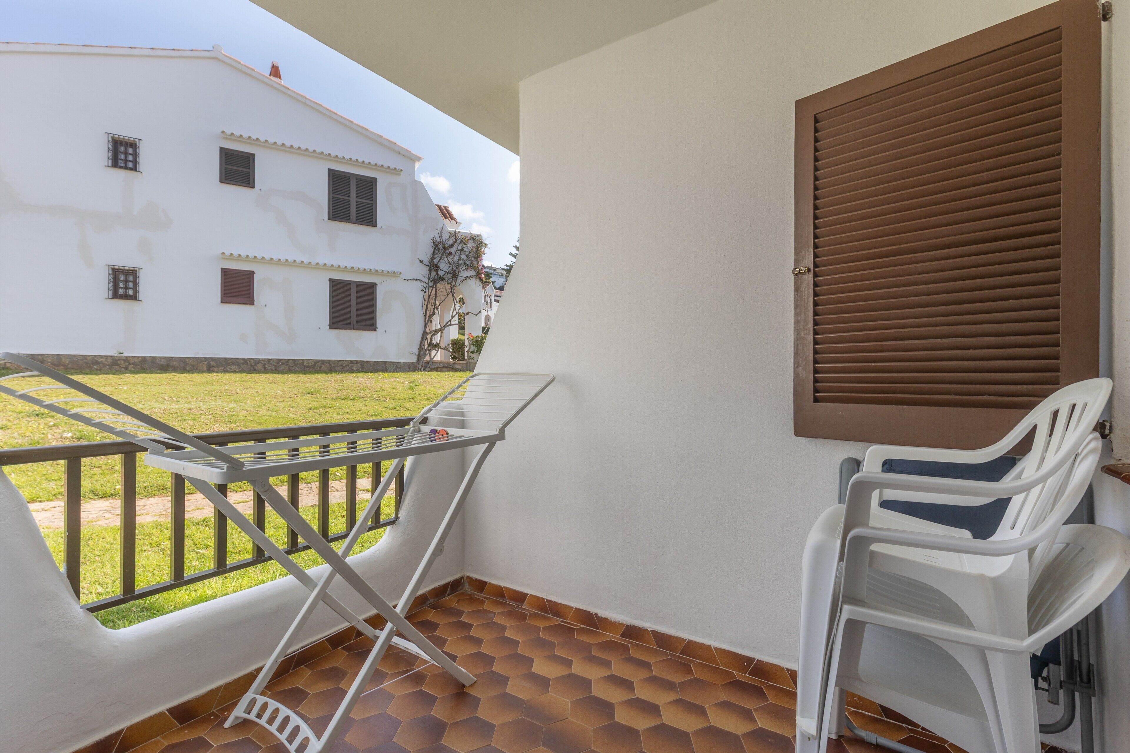 A balcony with a metal chair, a white plastic chair, and a metal table.