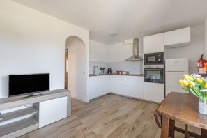 Een moderne keuken met witte kasten, een magnetron, oven en een flatscreen televisie.
