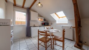 A kitchen with a skylight, wooden beams, a dining table with chairs, and a white refrigerator. - 30m² F1 Apartment in the Hautes-Vosges (Rochesson)