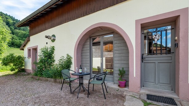 A building with a gravel patio, a table with chairs, and a door with a metal gate. - 30m² F1 Apartment in the Hautes-Vosges (Rochesson)