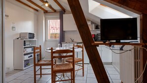 A kitchen with a dining table, chairs, a microwave, and a television. - 30m² F1 Apartment in the Hautes-Vosges (Rochesson)