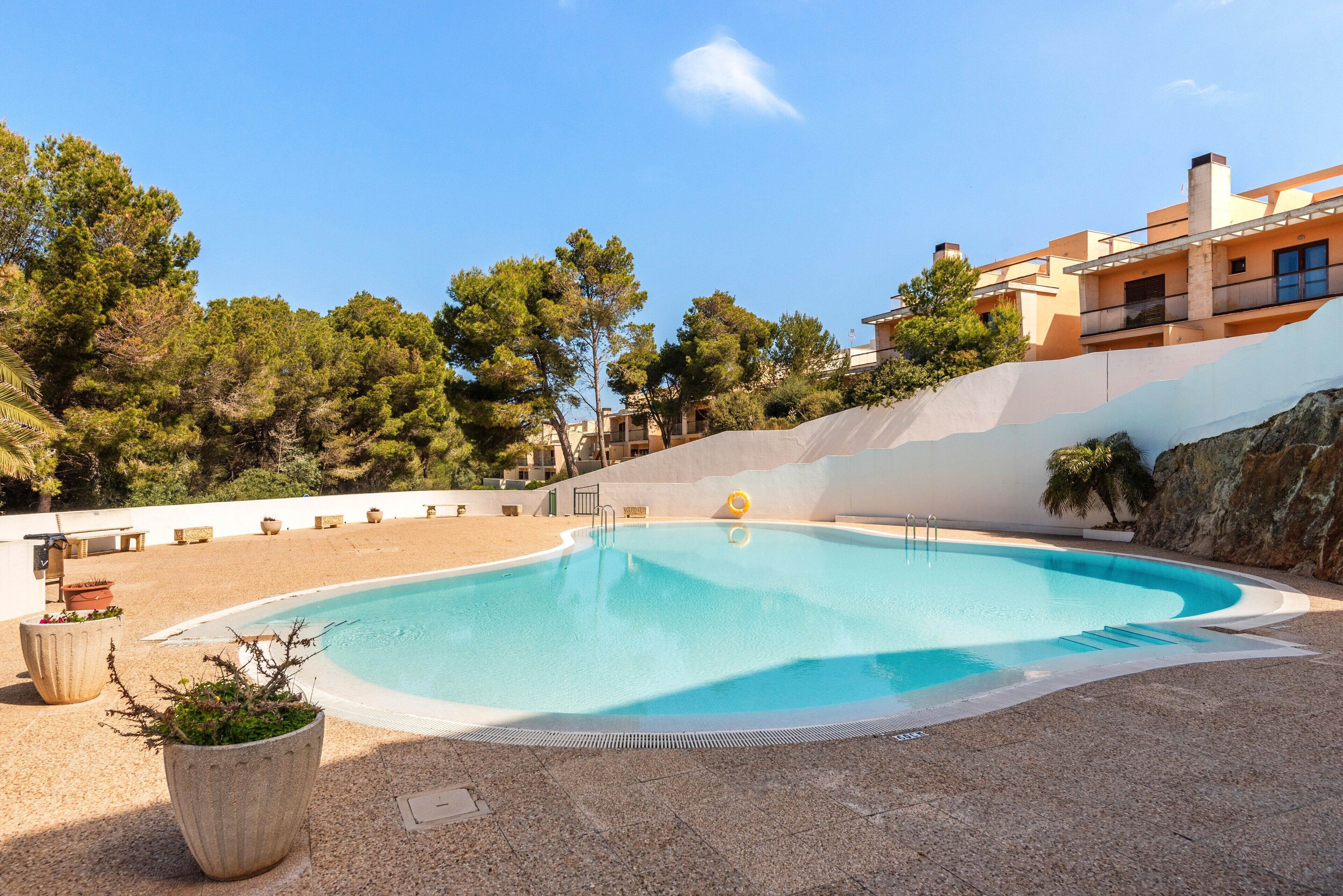 A swimming pool with a clear blue water, surrounded by a pebble deck, with a building in the background.