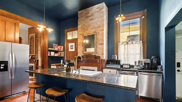 A kitchen with a central island, bar stools, a refrigerator, a dishwasher, and a brick wall.