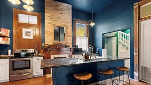 A kitchen with a wooden island, bar stools, a brick wall, and a view of a staircase.