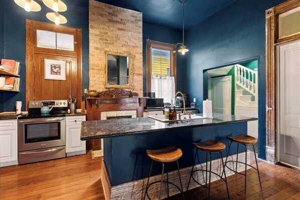 A kitchen with a wooden island, bar stools, a brick wall, and a view of a staircase.