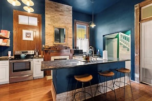 Une cuisine avec un Ăźlot central en bois, des tabourets de bar, un mur en briques et une vue sur un escalier.