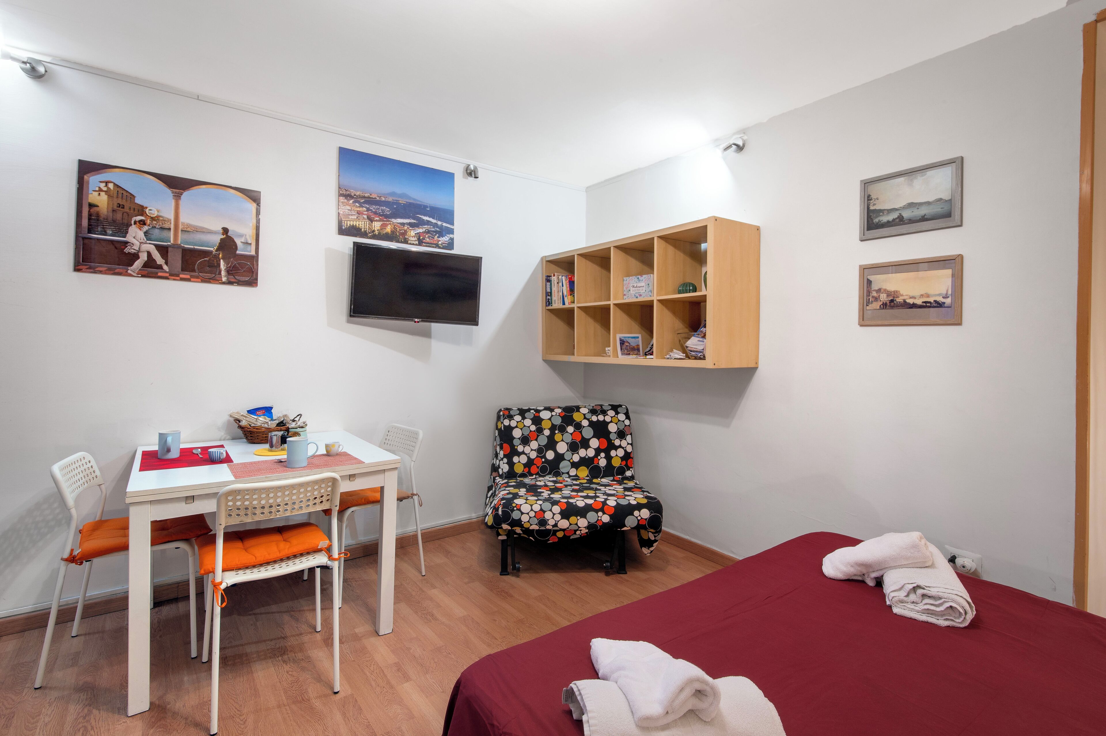 Una habitación con una cama, un escritorio con sillas, un televisor y estantes en la pared.