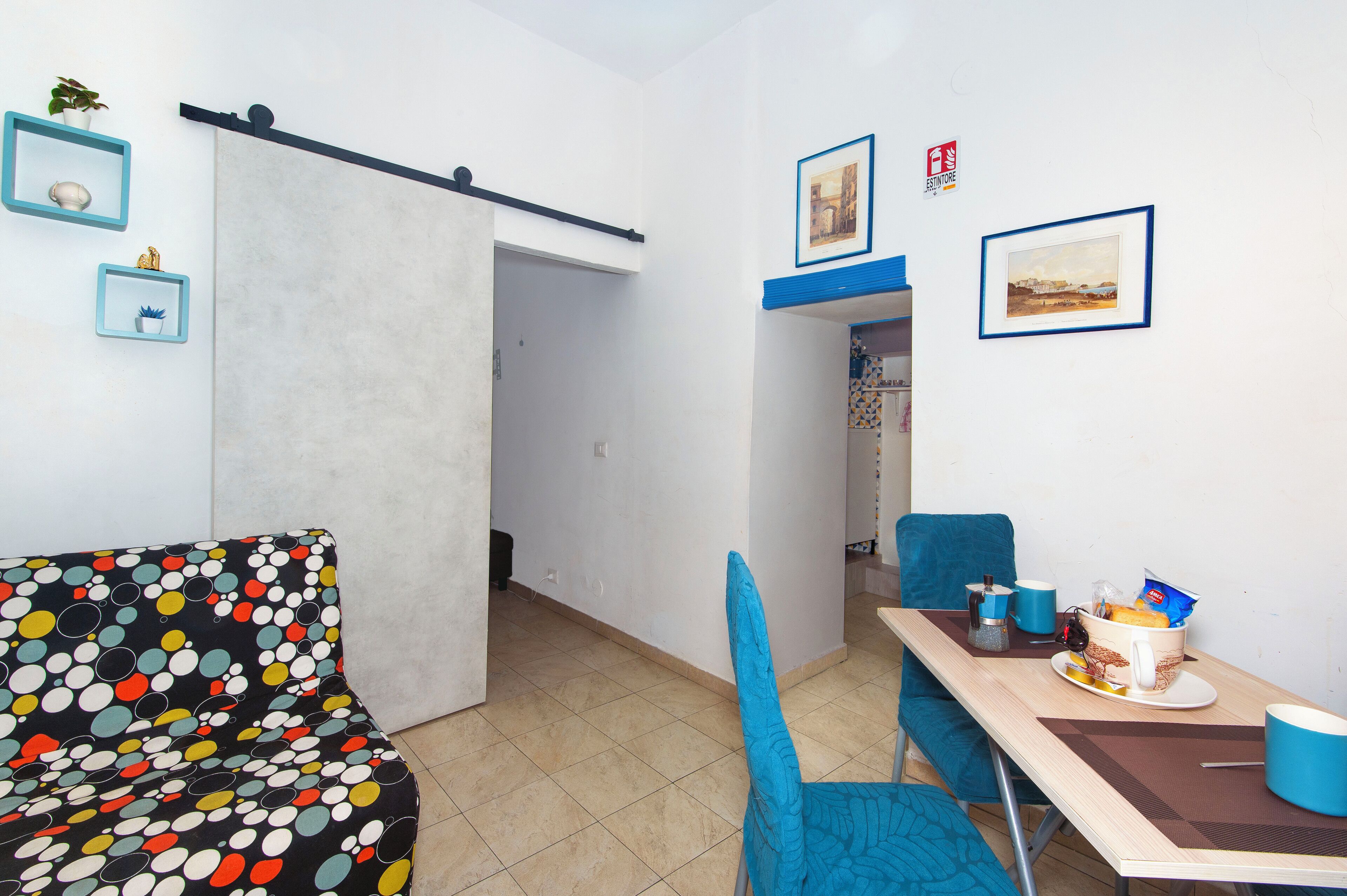 Una habitación con sofá, una mesa de comedor con sillas y una cocina visible a través de una puerta abierta.