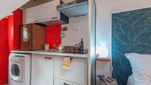 Une cuisine compacte équipée d’un lave-linge, d’une cuisinière et d’un petit plan de travail sur lequel sont disposés divers objets.