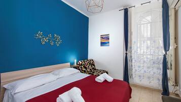 A hotel room with a bed, a chair, a wall art piece, and a window with curtains.