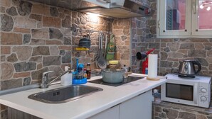 Une cuisine avec un dosseret en pierre, un évier, une cuisinière et un four à micro-ondes.