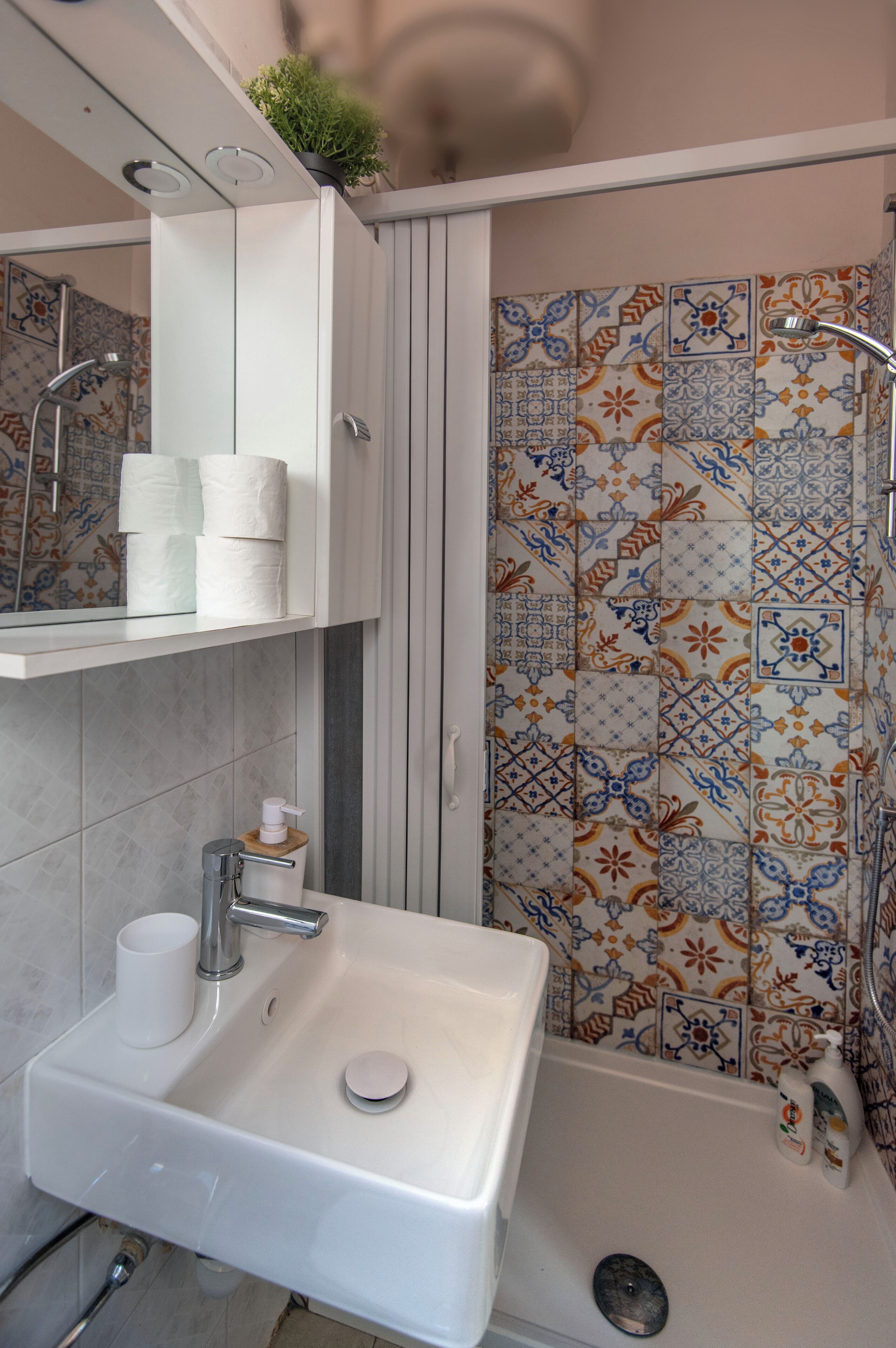 Ein Badezimmer mit weißem Waschbecken, Spiegel, Dusche und einer gefliesten Wand mit Blumenmuster.