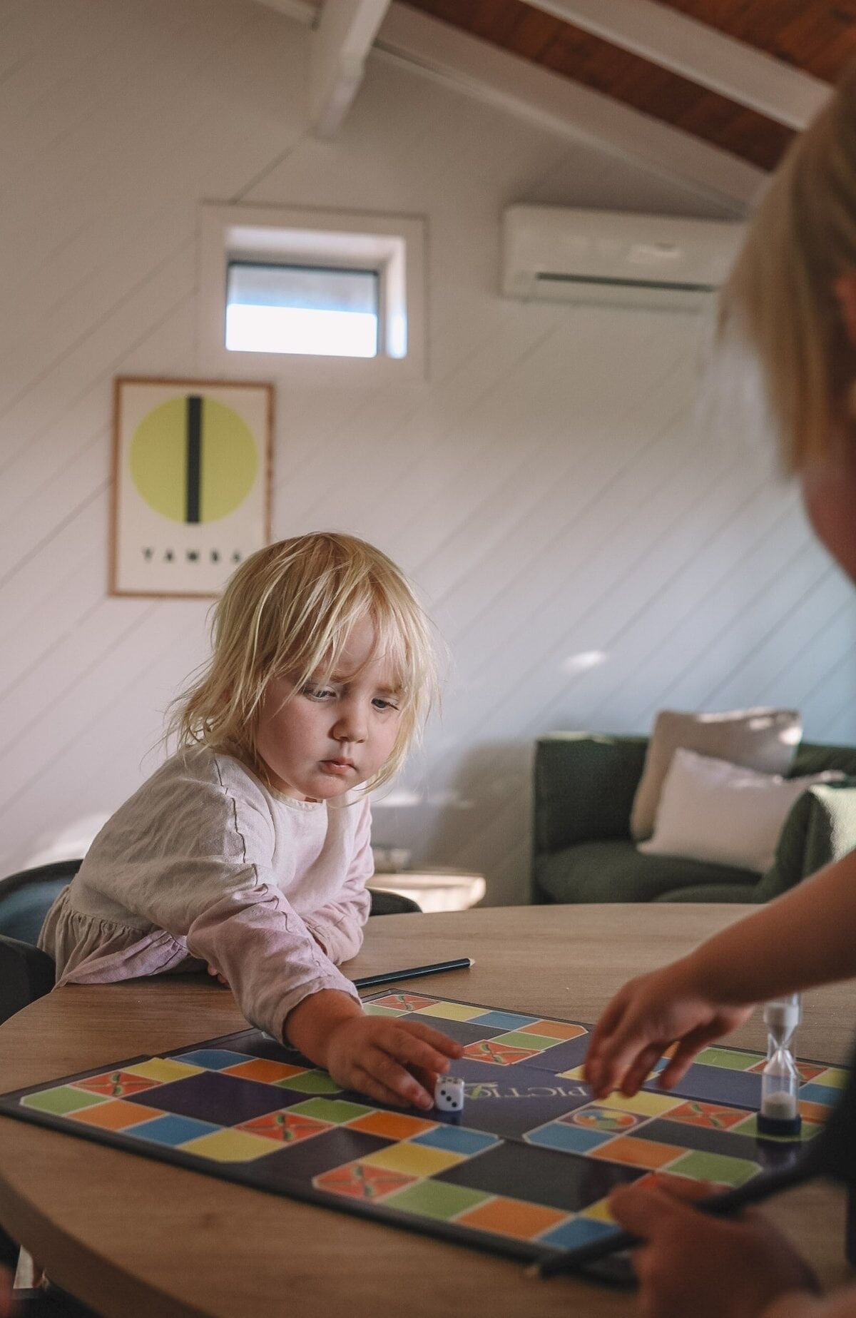 Et barn leger et brætspil ved et træbord i et rum med skråvægge og et vindue.
